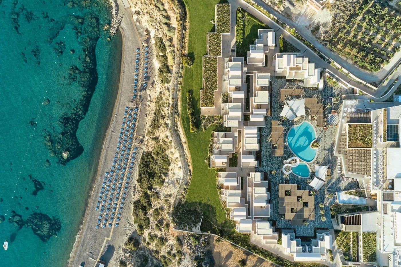 Drohnenaufnahme des ROBINSON Ierapetra: Das moderne Resort liegt direkt am Strand mit Blick auf türkisblaues Meer, Poolanlage und weitläufige Gartenflächen.