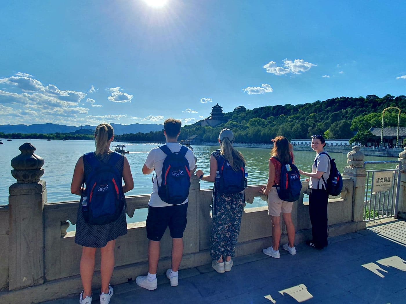 Teilnehmer einer Gebeco-Gruppenreise stehen am Ufer eines Sees in Peking und blicken auf den Sommerpalast unter strahlend blauem Himmel.